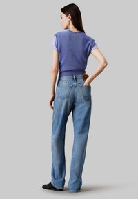 Top sin mangas de punto morado combinado con jeans de tiro alto en azul claro. Los jeans cuentan con bolsillos y una etiqueta de marca de cuero en la parte de atrás.