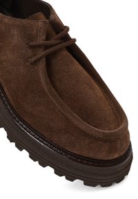 Brauner Velourslederschuh mit abgerundeter Spitze, zwei Ösen zur Schnürung und einer dicken, strukturierten Sohle mit leichtem Glanz und Nahtdetail.