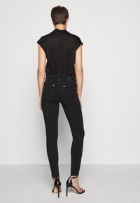 Jeans skinny de tiro alto en negro con una textura suave, bolsillos traseros y herrajes plateados, combinados con un top corto negro y tacones de aguja.