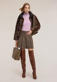 Giacca bomber con stampa leopardata, dolcevita lavanda, gonna plissettata a quadri, stivali marroni al ginocchio e borsa tote beige con manici trasparenti.