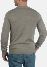 Maglione grigio lavorato a maglia con maniche lunghe, collo rotondo, polsini a coste e toppe sui gomiti. Abbinato a jeans di denim blu.