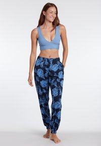 Svetlomodrý crop top s hlbokým výstrihom, skombinovaný s tmavomodrými nohavicami s tropickým vzorom listov v svetlomodrej farbe. Elastické manžety na nohaviciach.