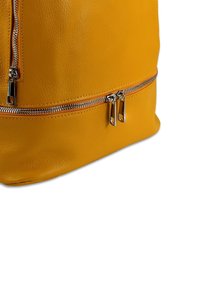 Geel leren rugzak met een gestructureerde afwerking, voorzien van zilveren ritsen en dubbele ritscompartimenten aan de voorkant en onderkant.