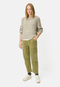 Grijze gebreide trui met een relaxte pasvorm, gecombineerd met olijfgroene cargobroek met meerdere zakken en een rechte pijp. Witte sneakers maken de look compleet.