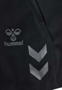 Zwarte sportshorts met een zachte textuur, voorzien van een grijs logo en chevronpatroonaccenten aan de zijkant. Inclusief ritsdetail.