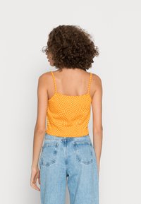 Top cropped xadrez laranja com alças finas, combinado com jeans de ganga de cintura alta de um azul claro. O top apresenta uma silhueta ajustada.