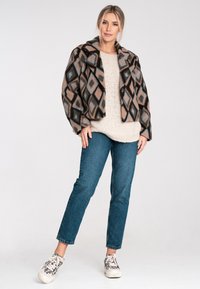 Wollmischung Jacke mit einem braun-schwarz-blauen Diamantmuster; oversized mit Kragen. Cremefarbener Strickpullover, blaue Jeans und gemusterte Sneakers.