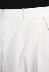 Jupe plissée blanche avec une texture lisse, dotée d'une fermeture éclair dissimulée à l'arrière. Lignes épurées et design minimaliste.