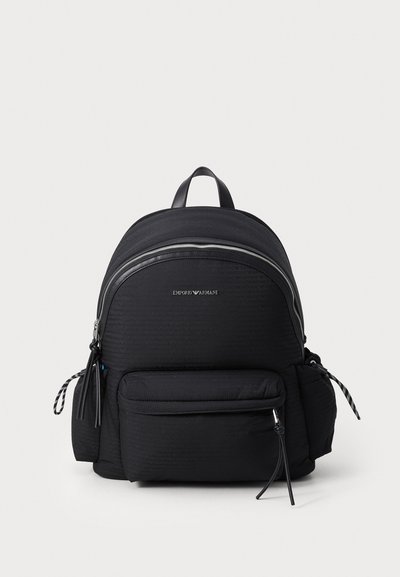 Sac à dos en nylon noir avec une surface texturée, fermeture éclair argentée, poche avant et bretelles réglables. Doté de détails de marque à l'avant.