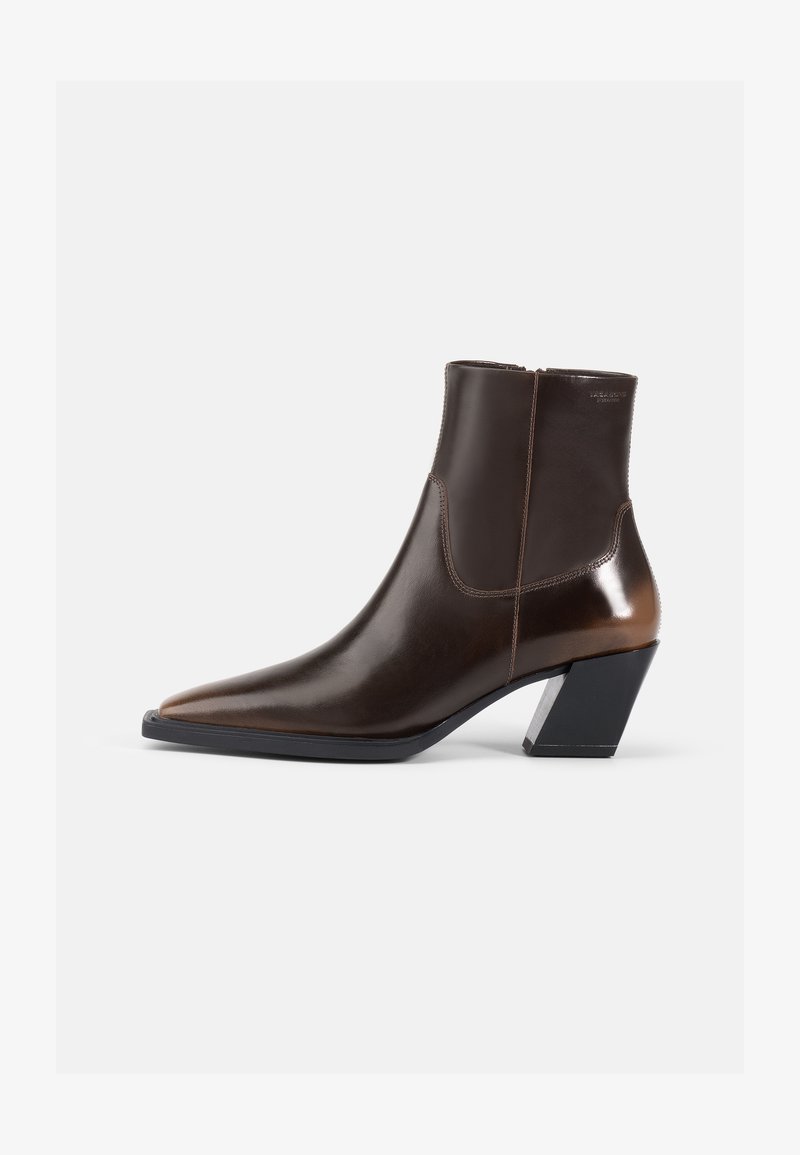 Bottine en cuir brun avec un bout pointu et un talon noir géométrique. Texture lisse avec un panneau contrastant et une fermeture éclair.