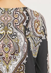 Dos du vêtement avec un motif cachemire complexe en noir, blanc, jaune, rose et marron sur le tissu.