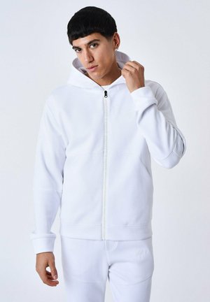 Sweat à capuche zippé blanc en tissu lisse avec capuche à cordon, poches latérales et accents de logo sur la fermeture éclair et la manche.