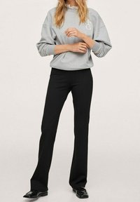 Grijze sweatshirt met een logo op de borst, gecombineerd met zwarte pantalon met rechte pijpen, voor een casual, gecoördineerde outfit.