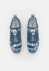 Baskets style denim dans diverses nuances de bleu avec une tige texturée, une semelle blanche et des lacets plats équipés d'un système de réglage à bascule.