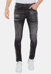 Zwarte denim skinny jeans met verwassen details, lichte vervaging en een vijf-pocket ontwerp, gecombineerd met witte sneakers.