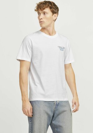 Witte katoenen T-shirt met korte mouwen, ronde halslijn en blauwe geborduurde tekst op de linkerborst. Draag het met lichtblauwe spijkerbroek.