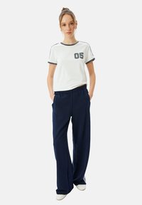 Hvid bomulds t-shirt med mørkegrå kant og et trykt "05", parret med marineblå løstsiddende sweatpants med sidelommer.
