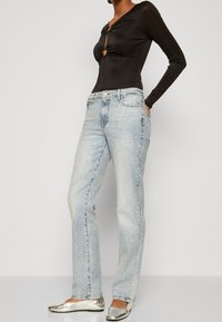 Body in lungo nero con scollatura a forma di cuore, abbinato a jeans azzurri chiari con accenti metallici e taglio dritto. Scarpe flat argentate.