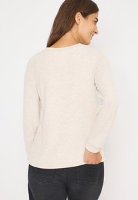 Pull beige clair en tissu doux, avec un col rond, des manches longues et une coupe décontractée, assorti à un jean noir.