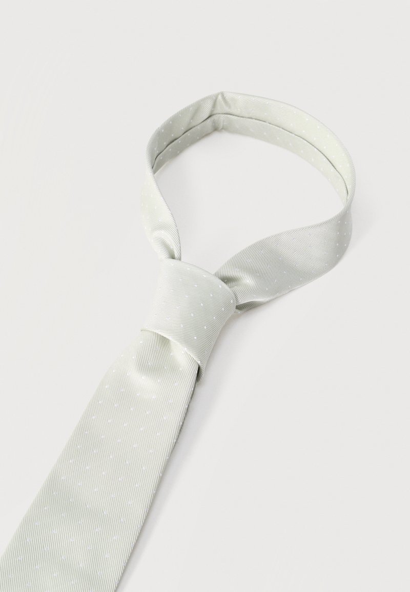 Lichtgrijze zijden stropdas met kleine witte stippen, geknoopt in een halve Windsor-knoop, afgebeeld tegen een effen witte achtergrond.