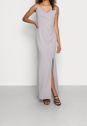 Nainen, joka käyttää vaaleanharmaata hihattomaa lattiaan ulottuvaa mekkoa, jossa on reiden korkuinen halkio, yhdistettynä mustiin remmikenkiin.