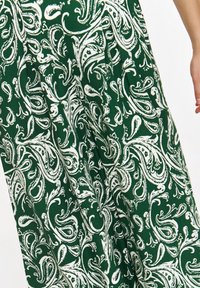 Zielony materiał z białym wzorem paisley, z drobnymi spiralami i kształtami. Materiał wydaje się miękki i lekki.
