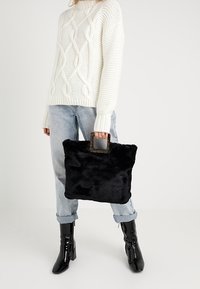 Svart faux fäll totes väska med rektangulär form och ett stort, transparent handtag; matchad med en vit kabelstickad tröja och ljus tvättade jeans.