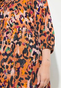 Vestido naranja con un estampado de leopardo en negro, púrpura y verde, con mangas fruncidas y detalles de falda plisada.