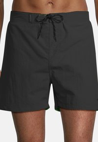 Zwarte zwemshorts met een trekkoord in de taille, gemaakt van lichtgewicht materiaal, met een contrasterende groene binnenkant en een eenvoudige, gladde textuur.