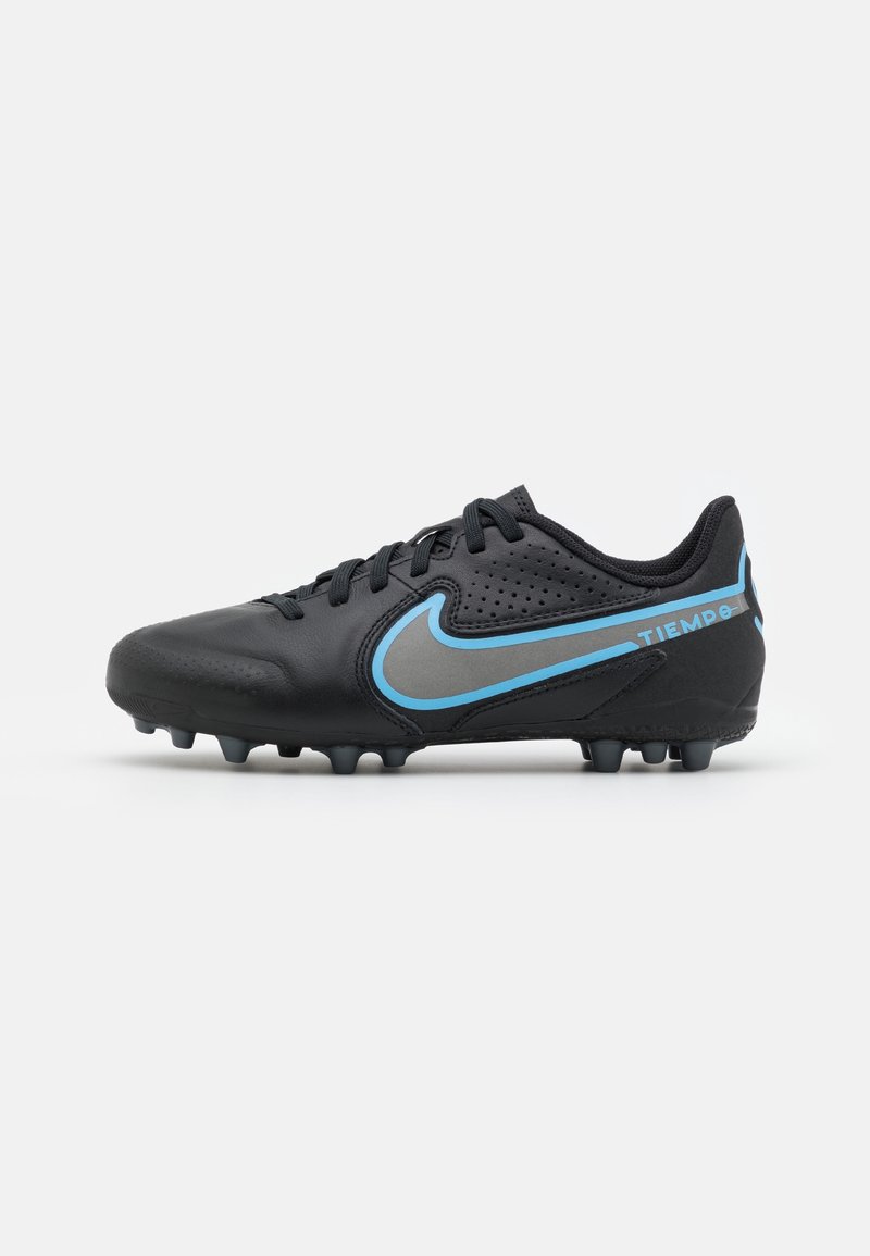 Botas de fútbol negras hechas de material sintético, con un diseño de swoosh en azul y gris, superficie texturizada y múltiples tacos para tracción.