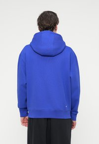 Μπλε φούτερ με μεγάλη, απαλή κουκούλα, ριμπ μανσέτες και τελείωμα, με μικρό λογότυπο κοντά στη μέση, κατασκευασμένο από υλικό fleece.