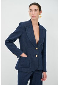 Blazer in denim scuro con colletto a rever, bottoni dorati, due tasche frontali e spalle strutturate. Tessuto liscio e design aderente.