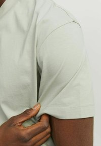 Camiseta de algodón verde claro con mangas cortas, que presenta una textura suave y un puño de manga ajustado. Detalle de costura sutil en el dobladillo.