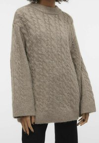 Beige knitted sweater with a cable pattern, crew neck, and wide sleeves. Soft texture and ribbed hem. Paired with black bottoms.