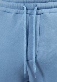 Jasnoniebieskie spodnie dresowe z teksturowanej tkaniny, z elastycznym pasem i bocznymi kieszeniami. Projekt obejmuje subtelny połysk oraz prążkowane akcenty.