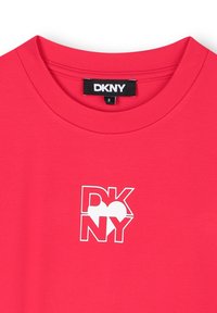 T-shirt en coton rouge avec un col rond, arborant un graphique du logo DKNY blanc sur le devant. Design simple avec une texture lisse.