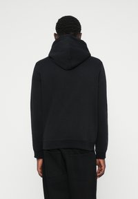 Sweat à capuche noir avec une capuche spacieuse et doublée, des poignets et un ourlet à côtes. Présente une texture lisse et un design minimaliste. Vue arrière montrée.