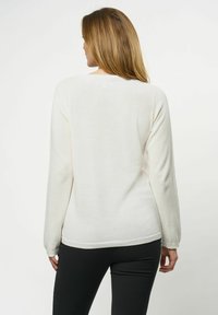 Kremfarget strikkegenser med lange ermer, rund utringning og ribbestrikkede mansjetter. Stoffet er glatt og lett med en subtil tekstur.
