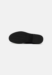 Black rubber shoe sole featuring a zigzag tread pattern. Smooth surface with a central logo and reinforced heel for durability.