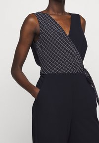 Lentopuku merivoimien tyyliin, jossa on kietaisusuunnittelu, ruudullinen vartalo-osuus ja sivuҙа. Silkkinen pinta, taskut; hihaton malli.