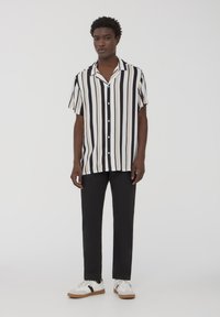 Camicetta a maniche corte a righe in nero, bianco e beige, con chiusura a bottoni. Abbinala a pantaloni neri e sneakers bianche con dettagli neri.