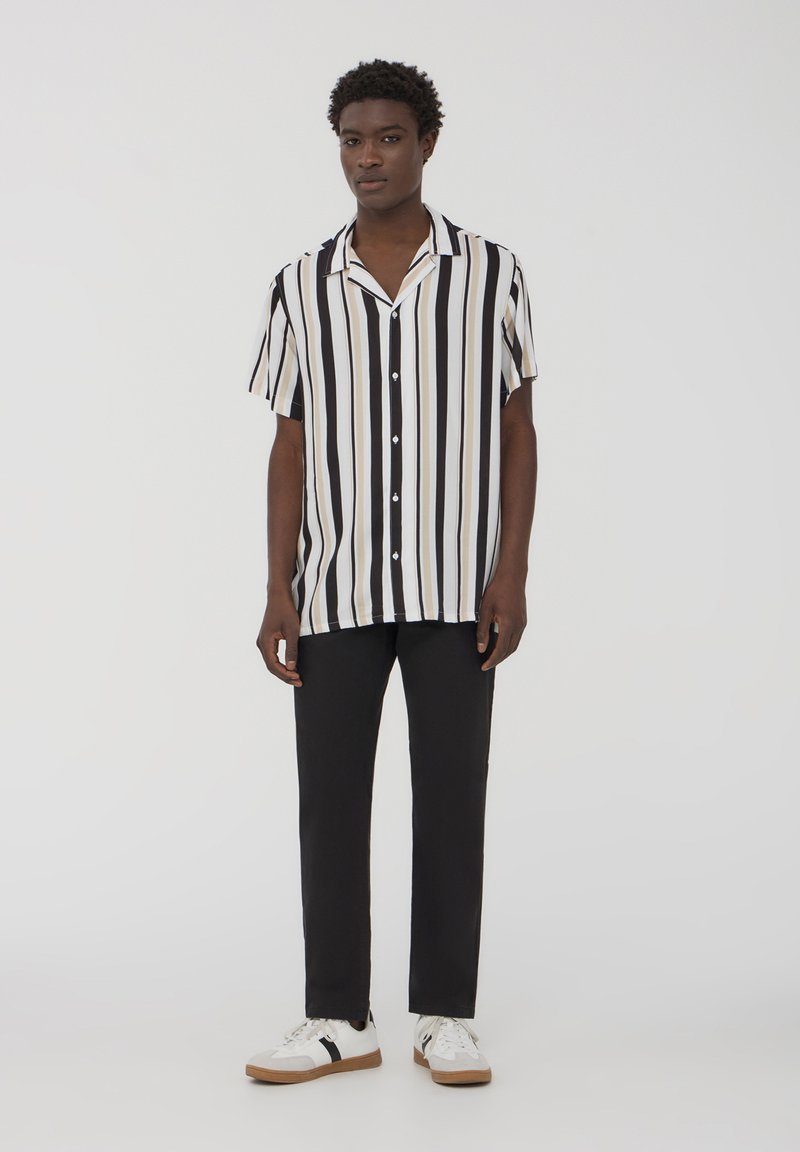 Camicetta a maniche corte a righe in nero, bianco e beige, con chiusura a bottoni. Abbinala a pantaloni neri e sneakers bianche con dettagli neri.