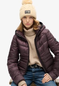 Veste en nylon violette avec un motif matelassé horizontal, fermetures éclair noires, associée à un pull en tricot beige et un bonnet avec un pompon.