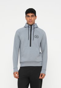 Lys grå hettegenser med rutemønster, glidelåslukking, snor og frontlomme; har en svart logo på brystet.