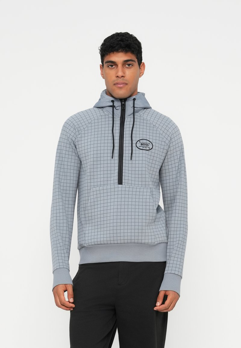 Lys grå hettegenser med rutemønster, glidelåslukking, snor og frontlomme; har en svart logo på brystet.