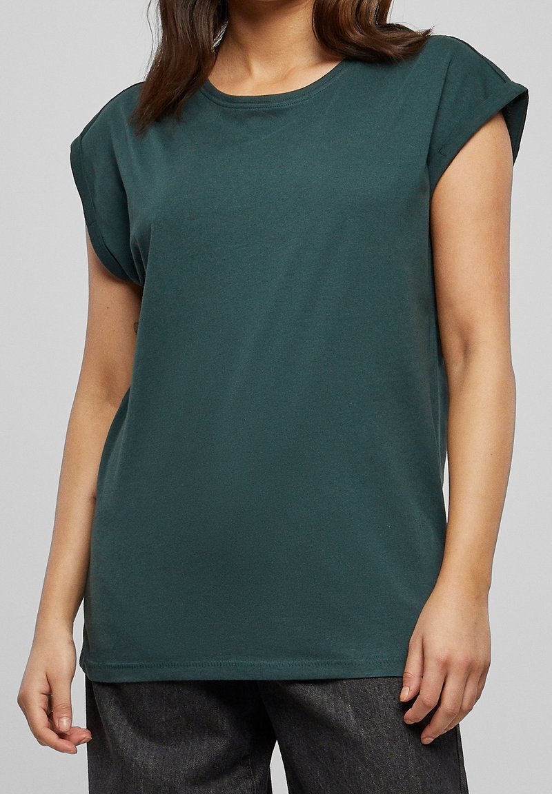 T-shirt en coton vert foncé avec des manches courtes retournées, col rond et coupe décontractée. Texture lisse, design uni, sans motifs ni accents visibles.