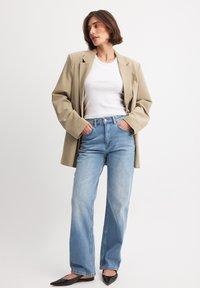 Beige oversized blazer, vit figurnära linne, ljusblå högmidjade jeans och svarta spetsiga ballerina skor. Texturerade tyger med avspänt snitt.
