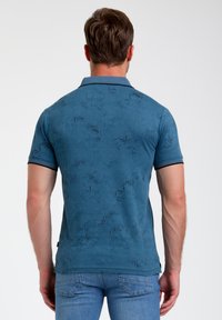 Polo bleu en tissu texturé, avec un motif botanique noir subtil, à manches courtes et col côtelé, associé à un jean bleu.