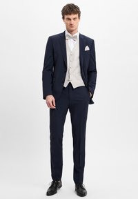 Herren Zweiteiler aus dunkelblauem Stoff, mit einer hell gemusterten Weste und schwarzen Abend-Schuhen. Taillierte Passform mit klassischem Design.