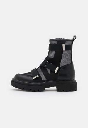 Czarny botek za kostkę wykonany z połączenia skóry i teksturowanej siateczki. Posiada regulowane paski, srebrne okucia oraz grubą, wytrzymałą podeszwę.